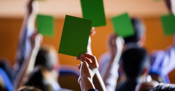 Rear View Of Business Executives Show Their Approval By Raising Hands At Conference Center